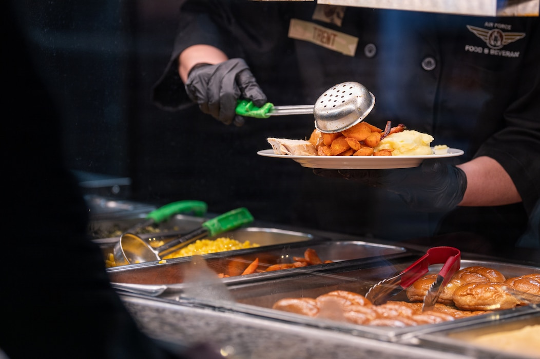 A U.S. Air Force Airman scoops food onto a plate at a buffet.