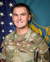 Man in U.S. Army uniform standing in front of two flags.
