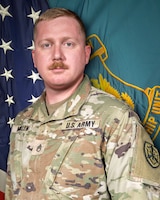 Man in U.S. Army uniform standing in front of two flags.