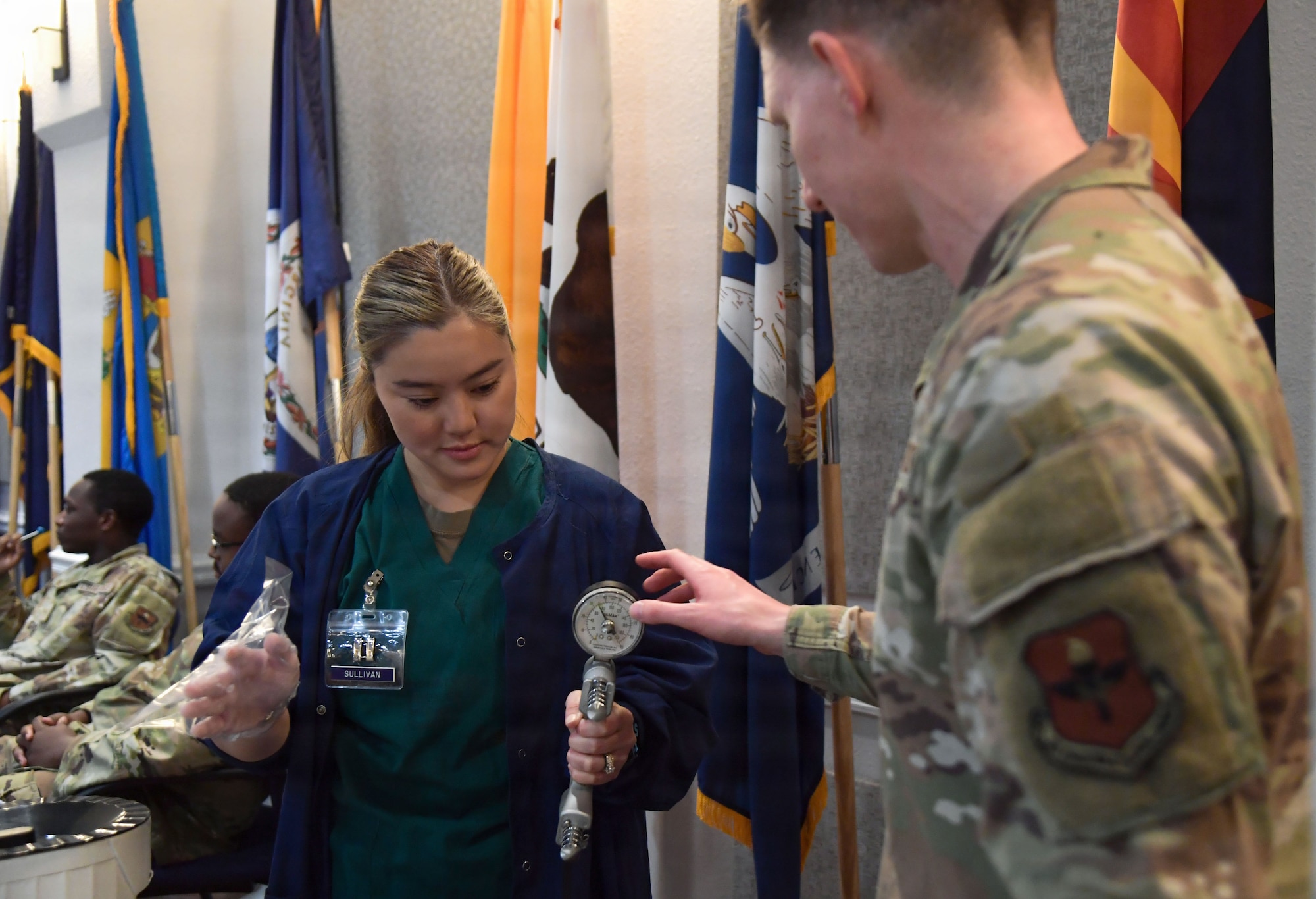 A man in military uniform speaks to a woman about a hand grip strength device.