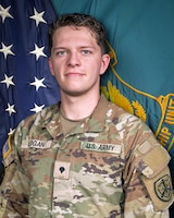 Man in U.S. Army uniform standing in front of two flags.