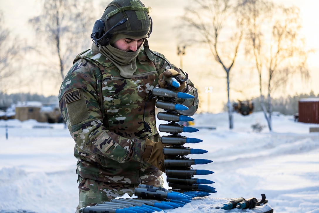 A soldier wearing a camouflage military uniform and headgear prepares ammunition for a training exercise.