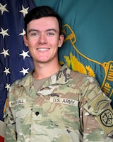 Man in U.S. Army uniform standing in front of two flags.