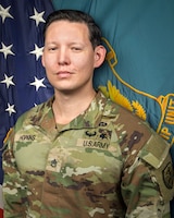 Man in U.S. Army uniform standing in front of two flags.