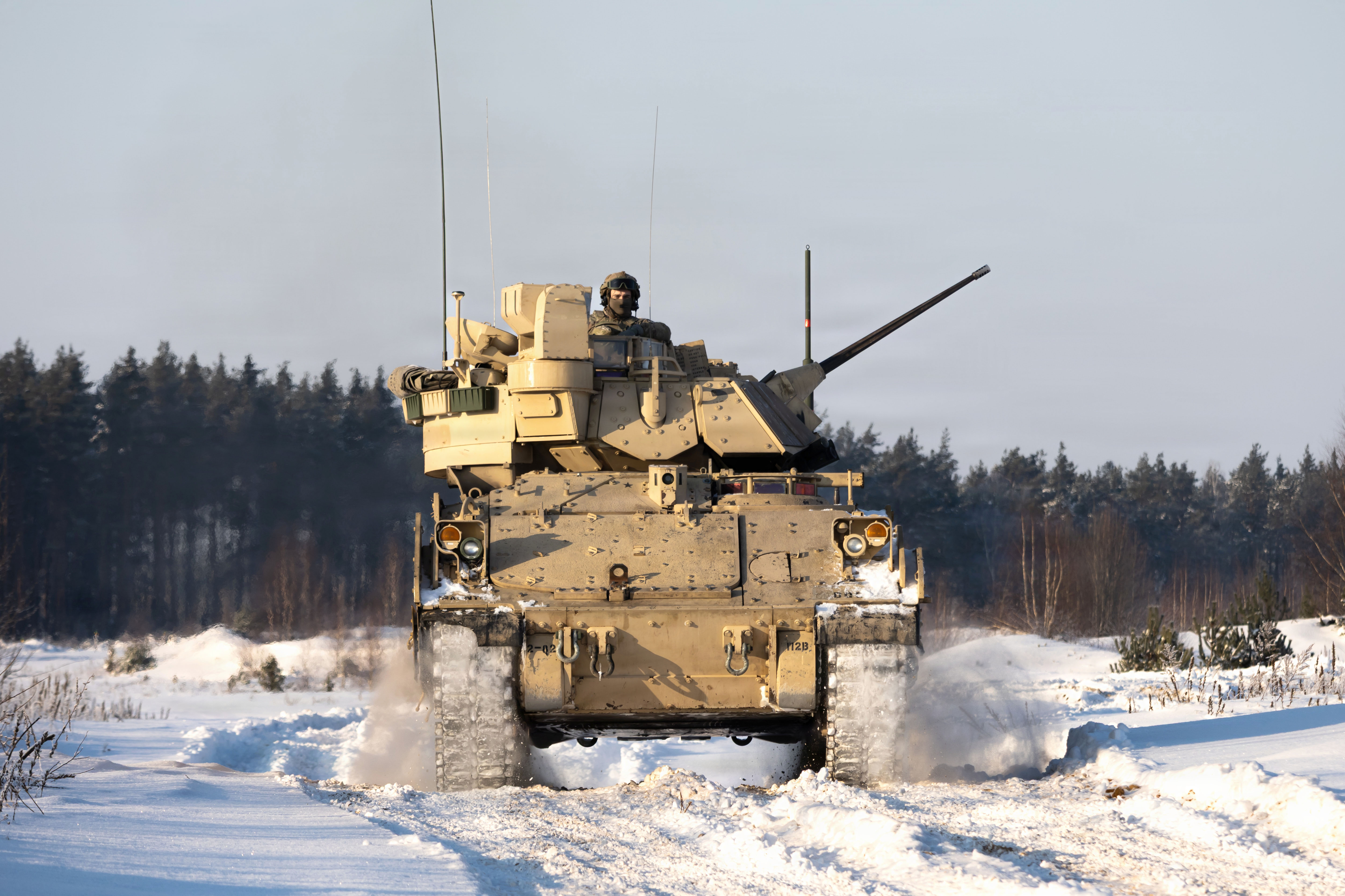 A soldier looks out from a tank traversing a snow-convered terrain.