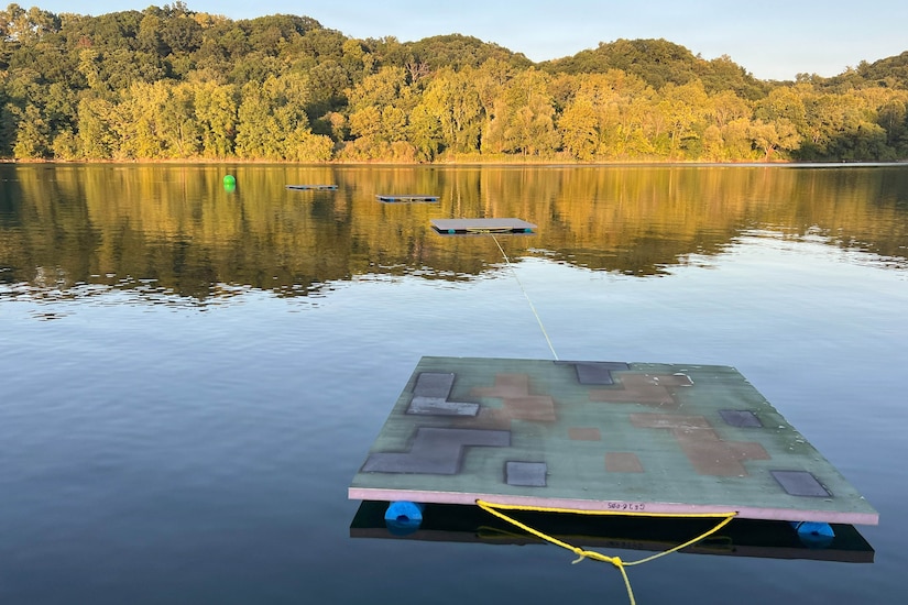 Metal camouflage panels float in a body of water surrounded by trees.