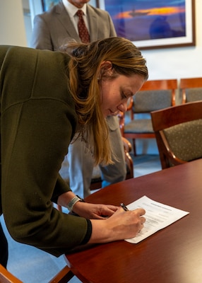 251216-N-IX644-1007 (Dec. 16, 2025) FALLS CHURCH, Va. Genevieve Landers, a native of Annandale, Virginia, and a program support specialist for the Navy Medicine Civilian Corps, signs the oath of office paperwork on Dec. 16, 2025. The Navy Medicine Enterprise's 44,000+ talented and ready forces optimize health readiness, deliver quality healthcare, and provide global expeditionary medical support to warfighters. (U.S. Navy photo by Mass Communication Specialist 2nd Class Sasha Ambrose)