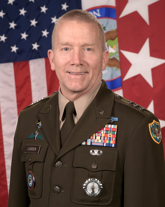 Lt. Gen. Thomas M. Carden poses in his military dress uniform for a portrait in front of the U.S. flag and a general's flag.