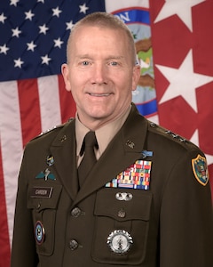 Lt. Gen. Thomas M. Carden poses in his military dress uniform for a portrait in front of the U.S. flag and a general's flag.