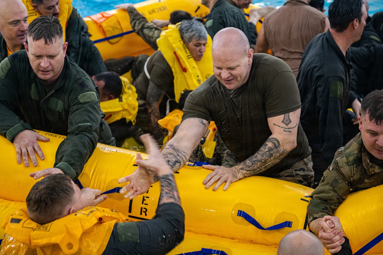 A group of people in military uniform sit in a life raft in a large indoor pool.