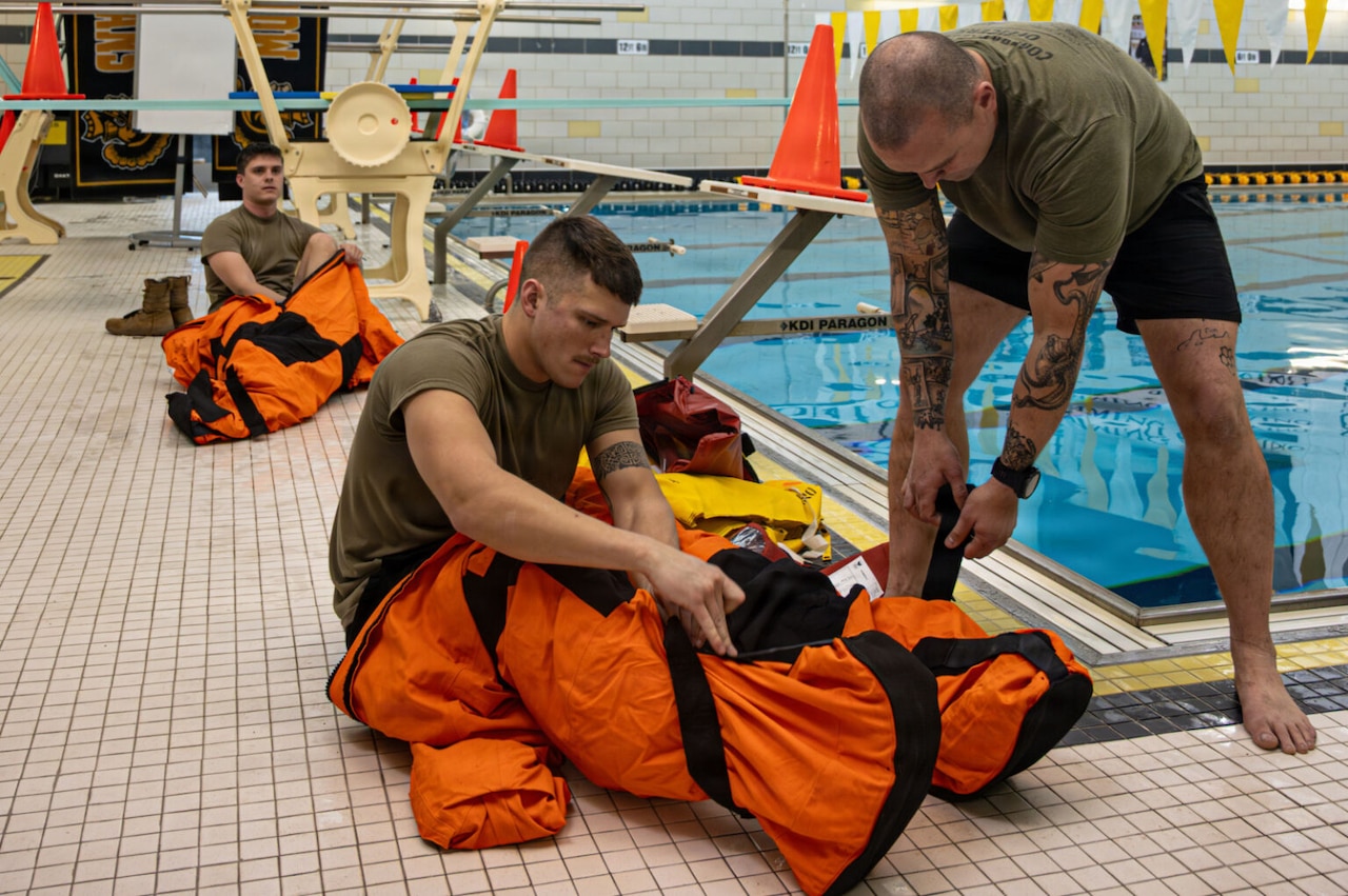 Three men put on orange water survival suits.