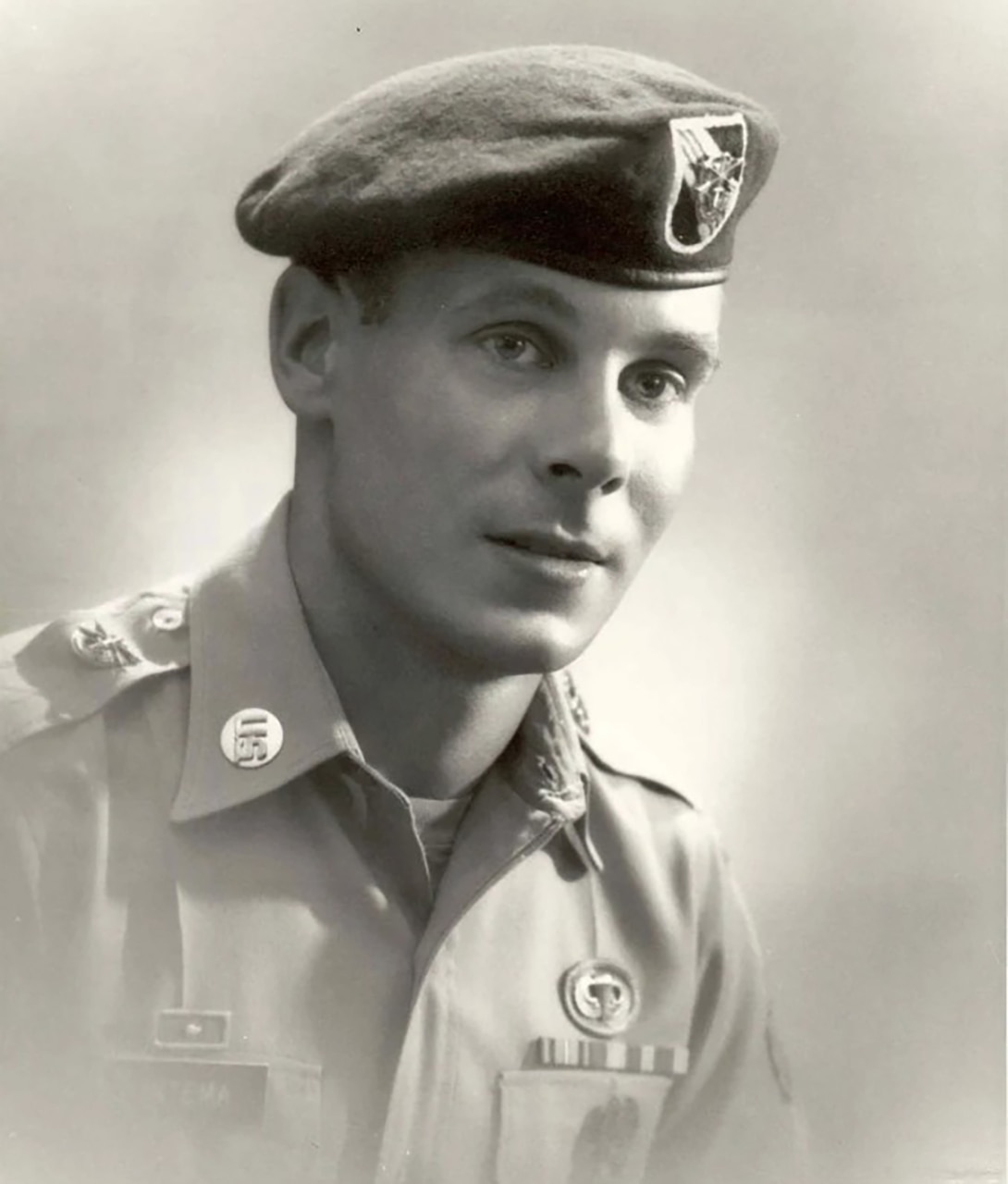 A man in a military dress uniform and beret poses for a photo.