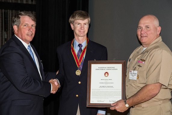 (center) Dr. Kerry Commander, NSWC PCD X Department Head, receives the National Defense Industrial Association Undersea Warfare Division Bronze Medal Award from (right) Rear Adm. Michael Jabaley, NAVSEA Program Executive Officer for Submarines in 2014. The conference aimed to address the Navy's key core competency mission of countering submarine and mine threats to the free and open flow of sea borne commerce and to the conduct of power projection from the sea. (courtesy photo)