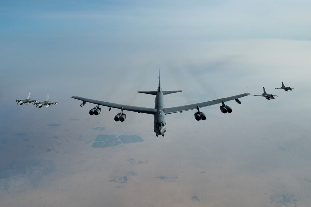 A large military bomber aircraft flies information with two military fighter jets flying on each side of it.