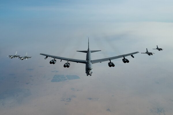 A large military bomber aircraft flies information with two military fighter jets flying on each side of it.
