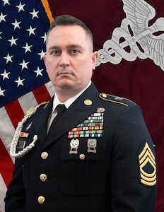 MSG Brandon Ruedi with the American Flag and MEDCOM Flag behind him.