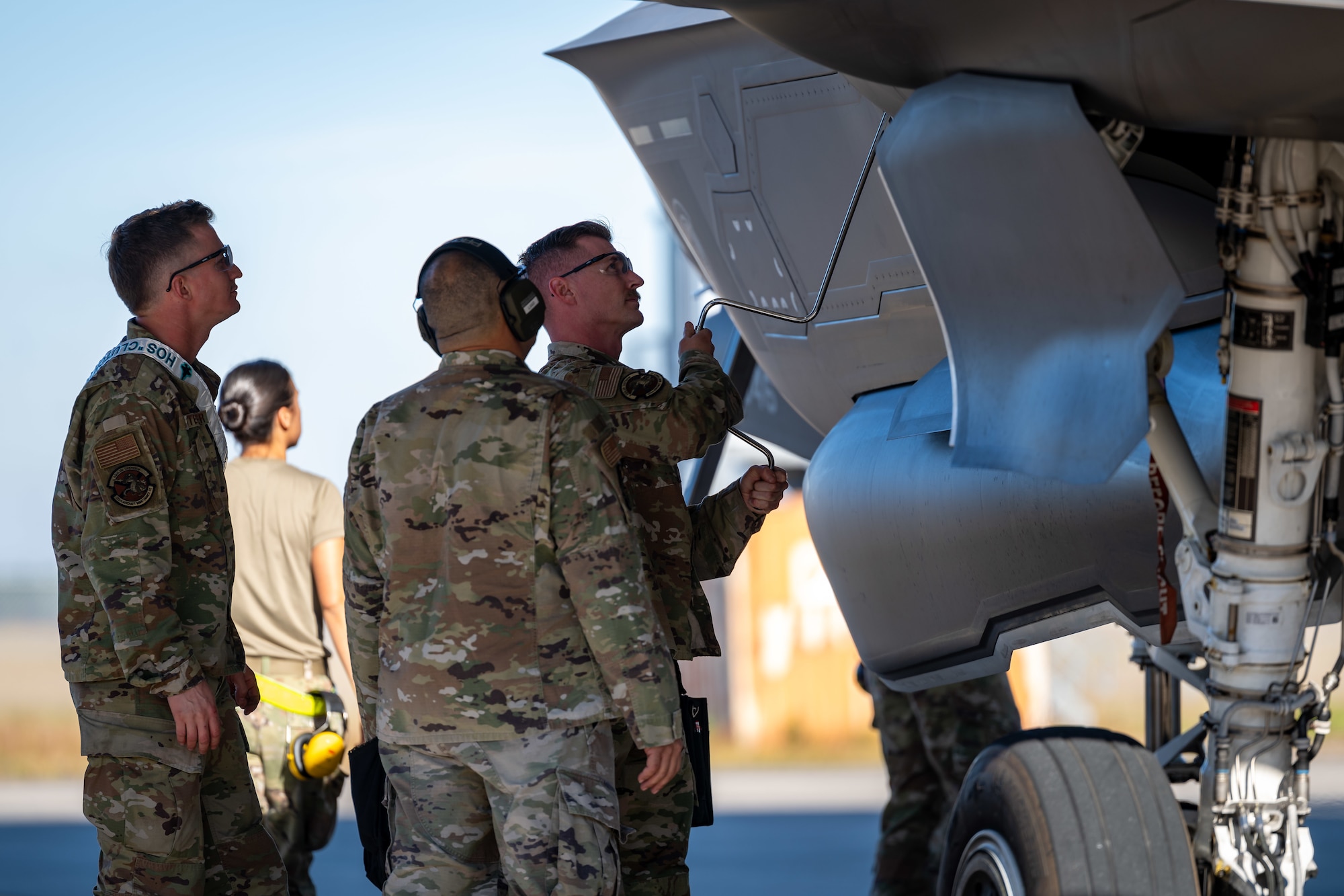 Three Airmen use a tool to remove a panel off of the F-35A aircraft.