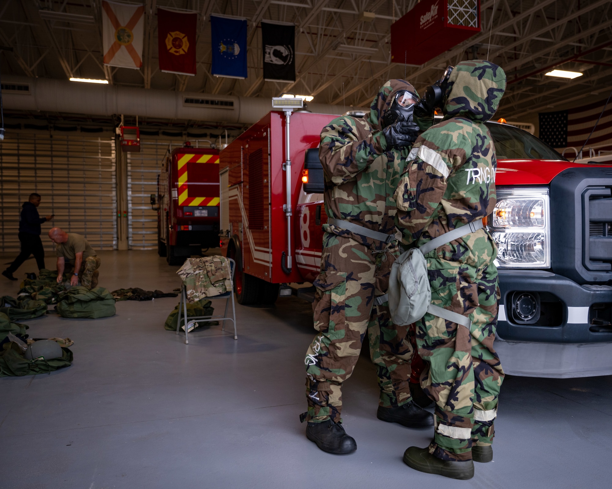 Two Airmen in MOPP gear check each other's suits to ensure it's being worn correctly.
