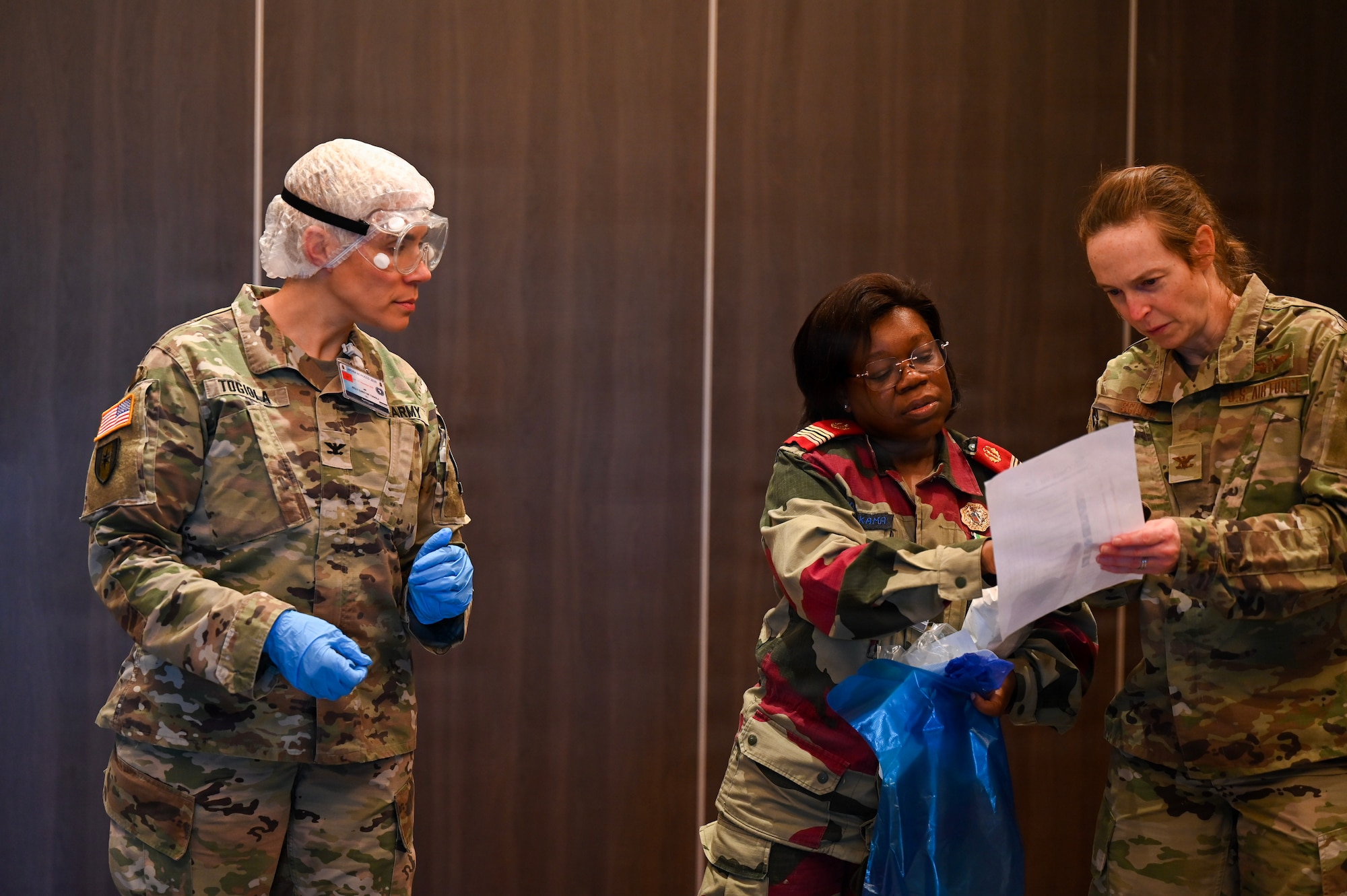 U.S. Army Col. Kelley Togiola, Southern European Task Force Africa Global Health Engagement chief, left, Gabon Armed Forces Col. Mbongo-Kama, Gabonese Army Health Services clinical pathologist, center, and U.S. Air Force Col. Brooke Sciuto, 155th Medical Group commander, right, work together to brief donning and doffing procedures of personal protective equipment during the African Partner Outbreak Response Alliance 2025 Workshop in Rabat, Morocco, Dec. 9, 2025. APORA 2025 brought together delegates from 30 African countries to come together and share lessons learned, techniques, tactics and procedures and discuss how to strengthen infectious disease outbreak response interoperability between military and civil organizations, countries and regional partners. (U.S. Air Force photo by Capt. Benjamin Aronson) (This photo was altered for security purposes by blurring a security badge.)