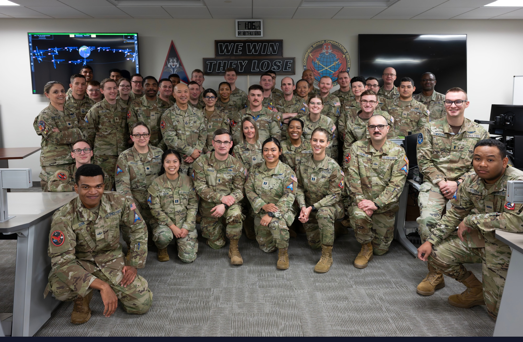 A group of military members stand and kneel together in a room