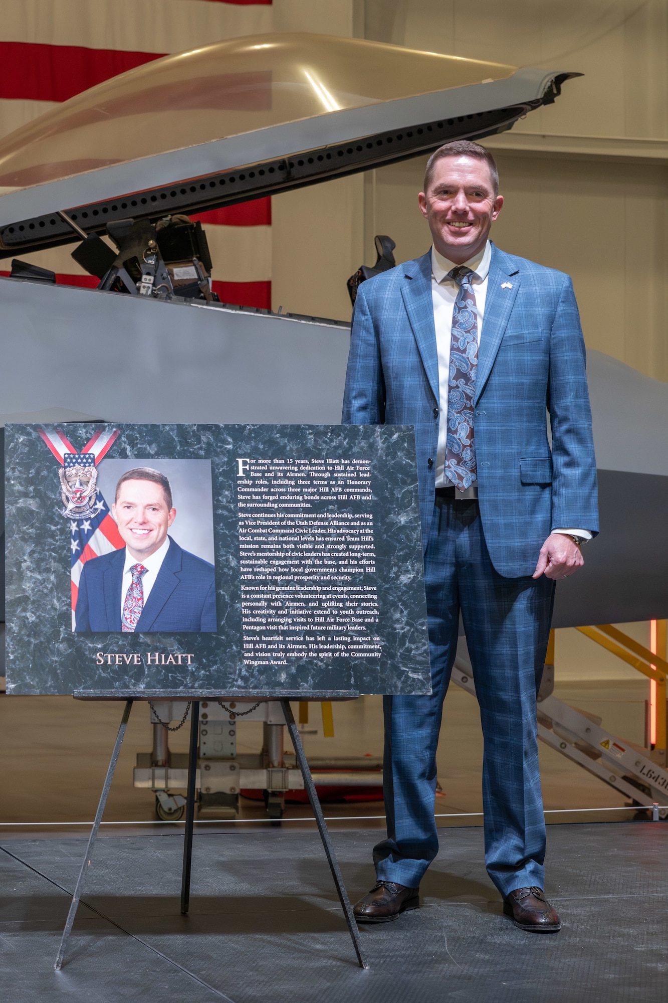 Steve Hiatt stands beside a replica Community Wingman Award plaque.