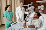 Kim Dang (left), registered nurse, and Army Maj. (Dr.) Mateo Houle (center), pulmonary critical care fellow, discuss a care plan with retired Army Sgt. Javier Arizola (right) at Brooke Army Medical Center, Joint Base San Antonio–Fort Sam Houston, Texas, June 18, 2025. TRICARE beneficiaries who are hospitalized in a network hospital can request transfer to BAMC by calling 210-916-2733. (DOW photo by Jason W. Edwards)