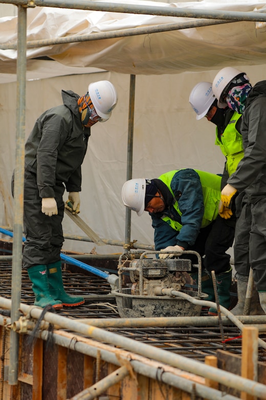 Contractor placing concrete at container storage shed on project site.