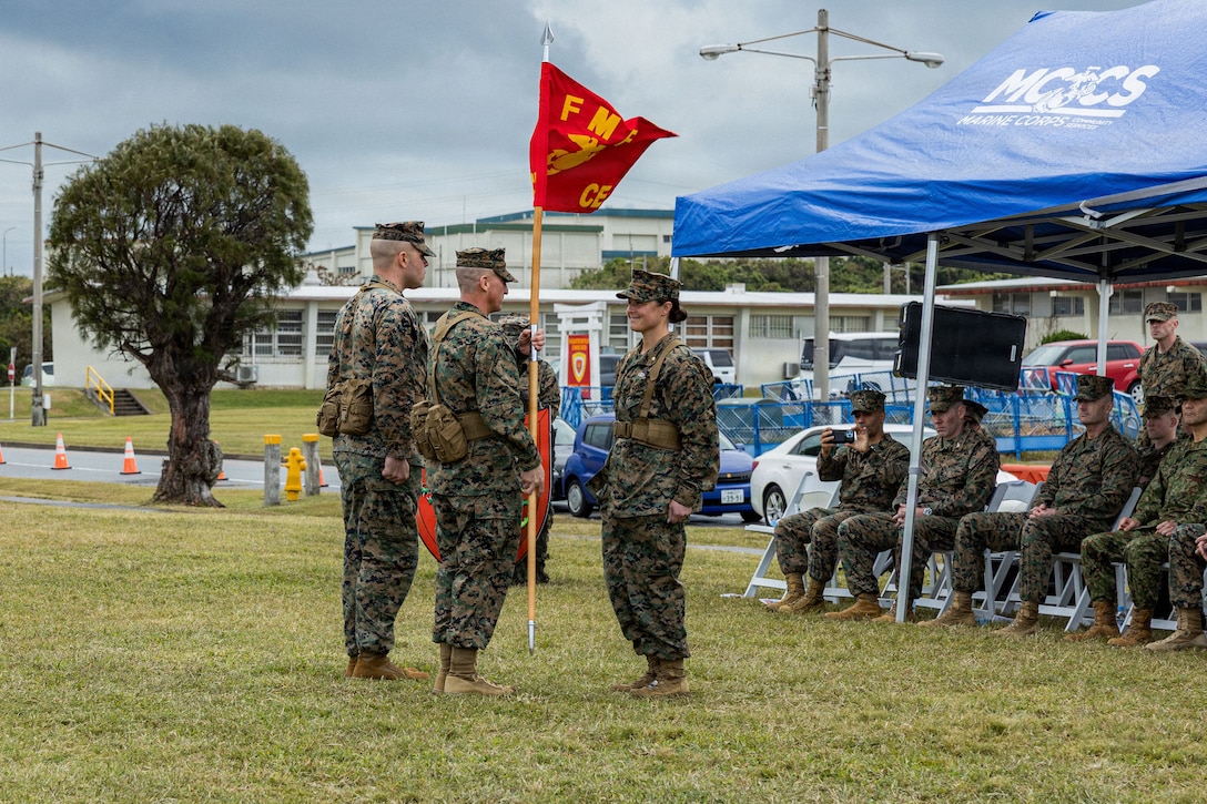 U.S. Marine Corps Brig. Gen. Robert Brodie, center, commanding general of 3rd Marine Expeditionary Brigade, passes the guide-on flag to Maj. Codi Mullen, headquarters company commander of 3rd MEB, during an activation ceremony for 3rd MEB at Camp Courtney, Okinawa, Japan, Jan. 13, 2026. The 3rd MEB established a new headquarters company to enhance their lethality by centralizing command and synchronizing readiness efforts across warfighting functions. (U.S. Marine Corps photo by Lance Cpl. Justin Cledera)