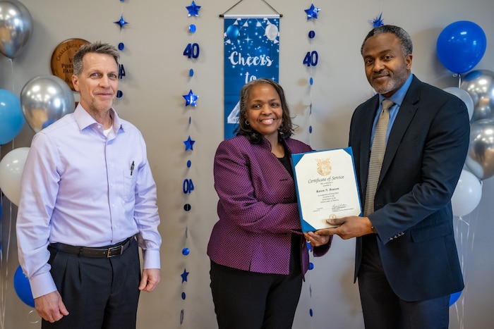 One woman and two men pose for a photo, the woman in the center receives a certificate from the man on the right