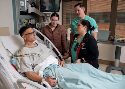 Patient lies in hospital bed while surrounded by three providers in scrubs.