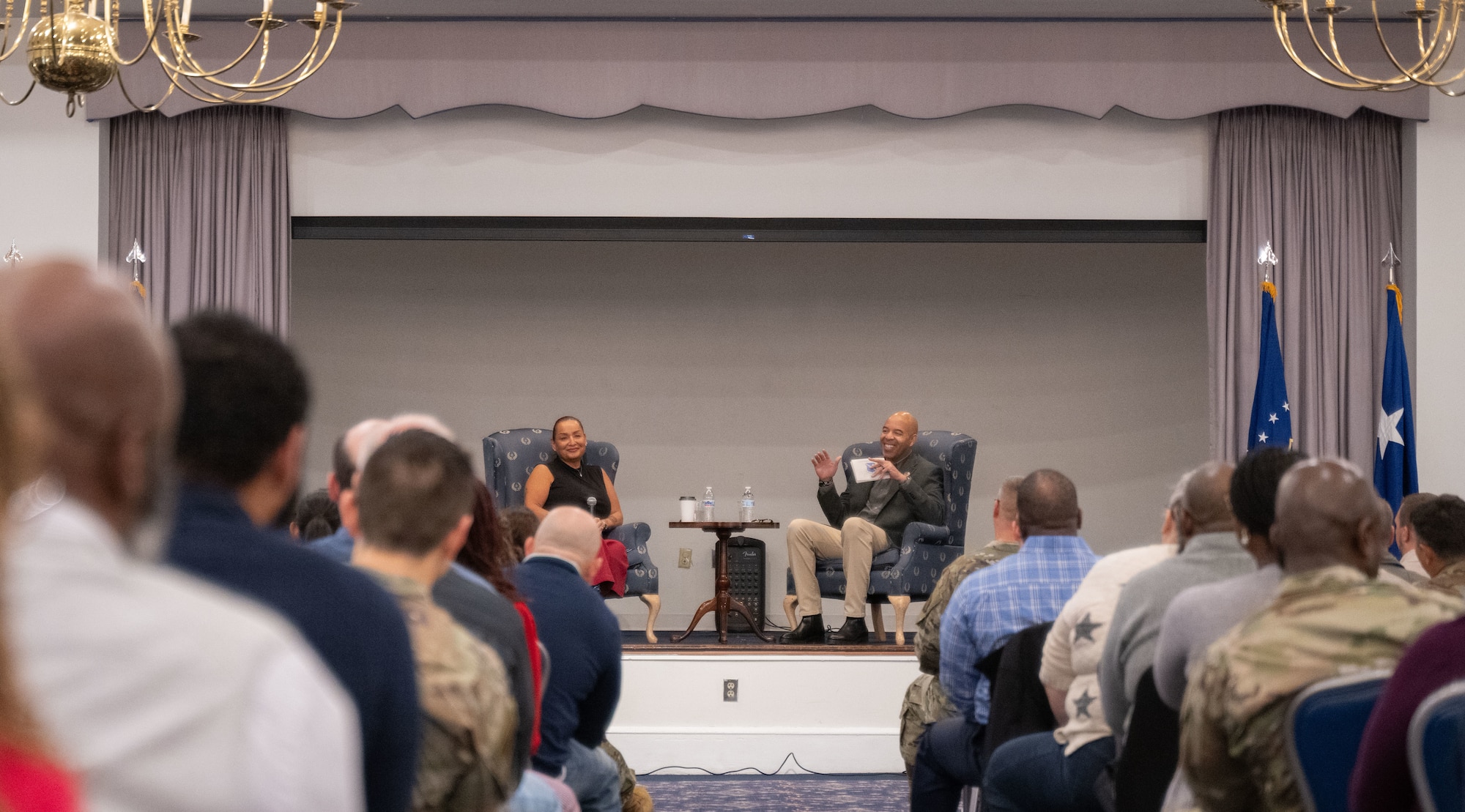 A crowd looks at a man and woman seated on a stage.