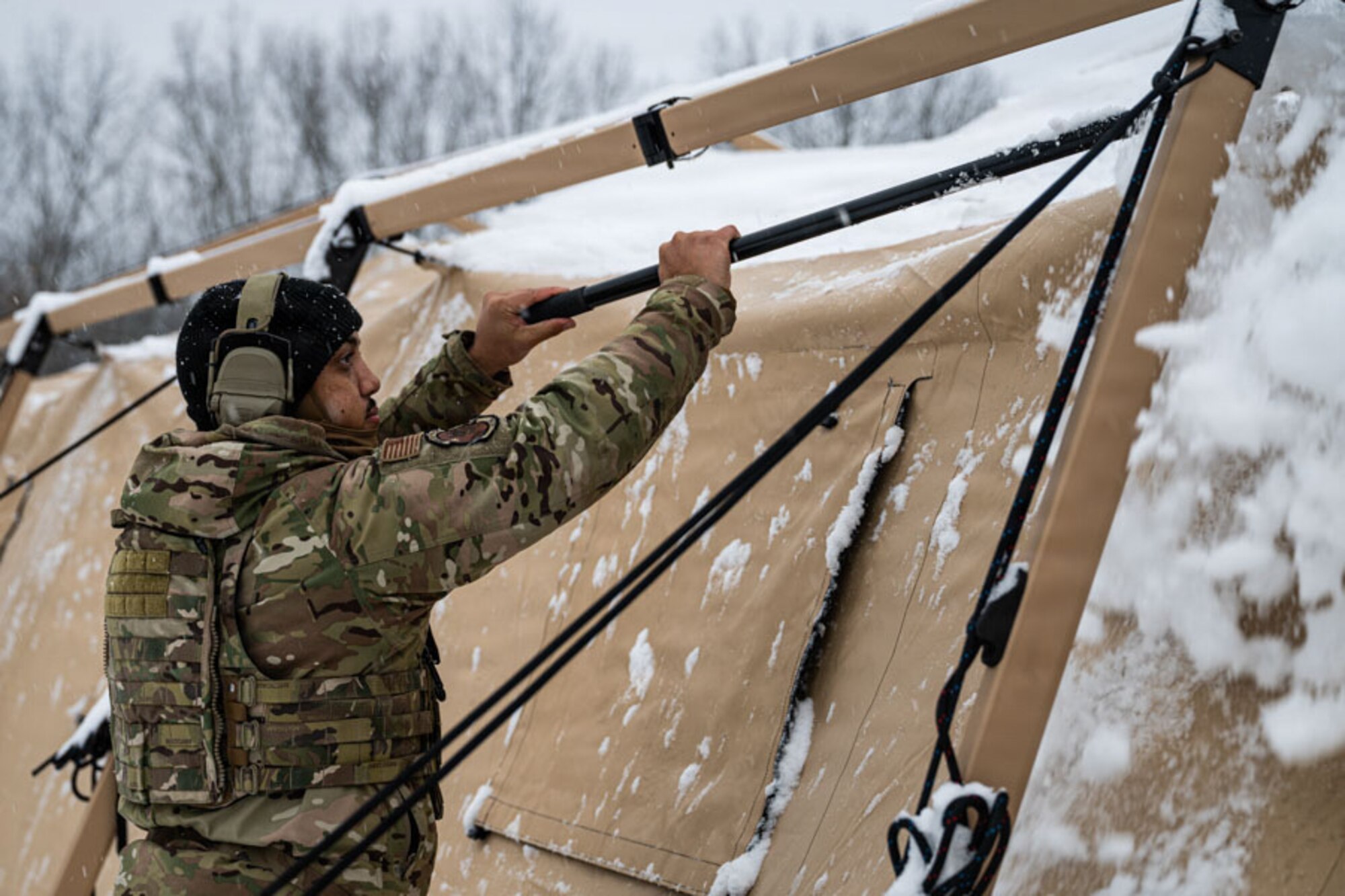 An Airman brushes snow off a tent.