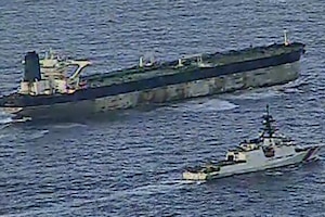 A Coast Guard ship cruises next to a larger vessel in an open body of water, as seen in grainy video footage from above.