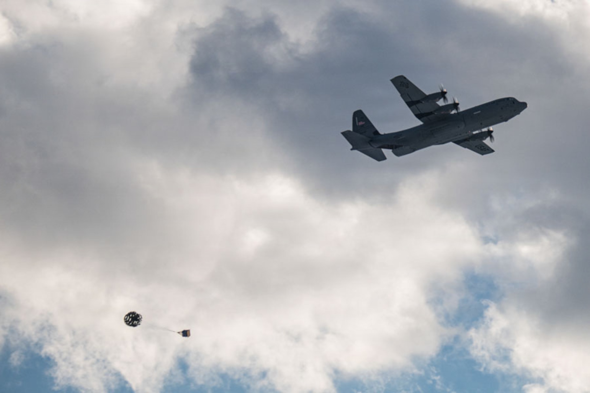 A cargo plane drops a pallet with a parachute.