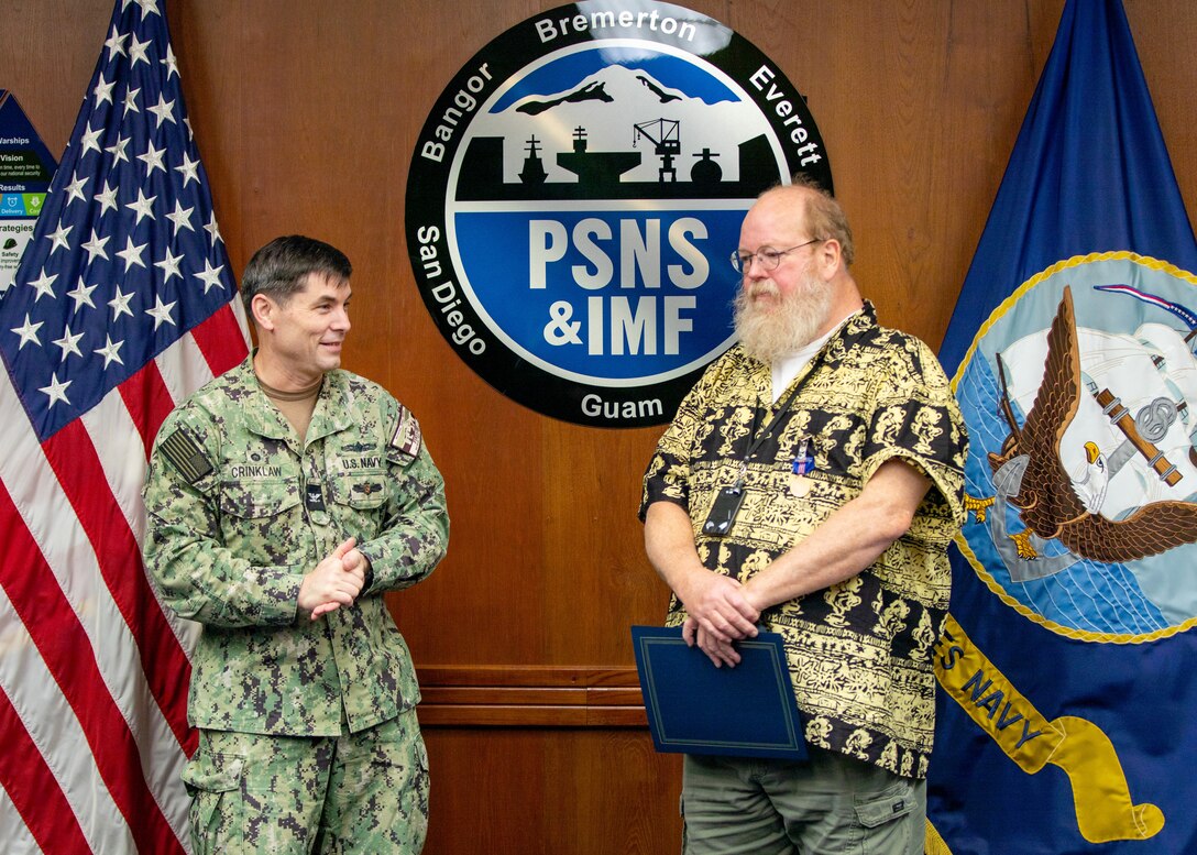 Capt. JD Crinklaw, commander, Puget Sound Naval Shipyard & Intermediate Maintenance Facility, presents Daniel Hager, senior engineering technician, Code 296, Combat Systems Engineering and Planning Division, with a Meritorious Civilian Service Award, Dec. 19, 2025, in Bremerton, Washington, for his work as "the Navy's foremost subject matter expert in precision optical alignment and 3D coordinate metrology." (U.S. Navy photo by Ben Hutto)