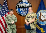 Capt. JD Crinklaw, commander, Puget Sound Naval Shipyard & Intermediate Maintenance Facility, presents Daniel Hager, senior engineering technician, Code 296, Combat Systems Engineering and Planning Division, with a Meritorious Civilian Service Award, Dec. 19, 2025, in Bremerton, Washington, for his work as "the Navy's foremost subject matter expert in precision optical alignment and 3D coordinate metrology." (U.S. Navy photo by Ben Hutto)