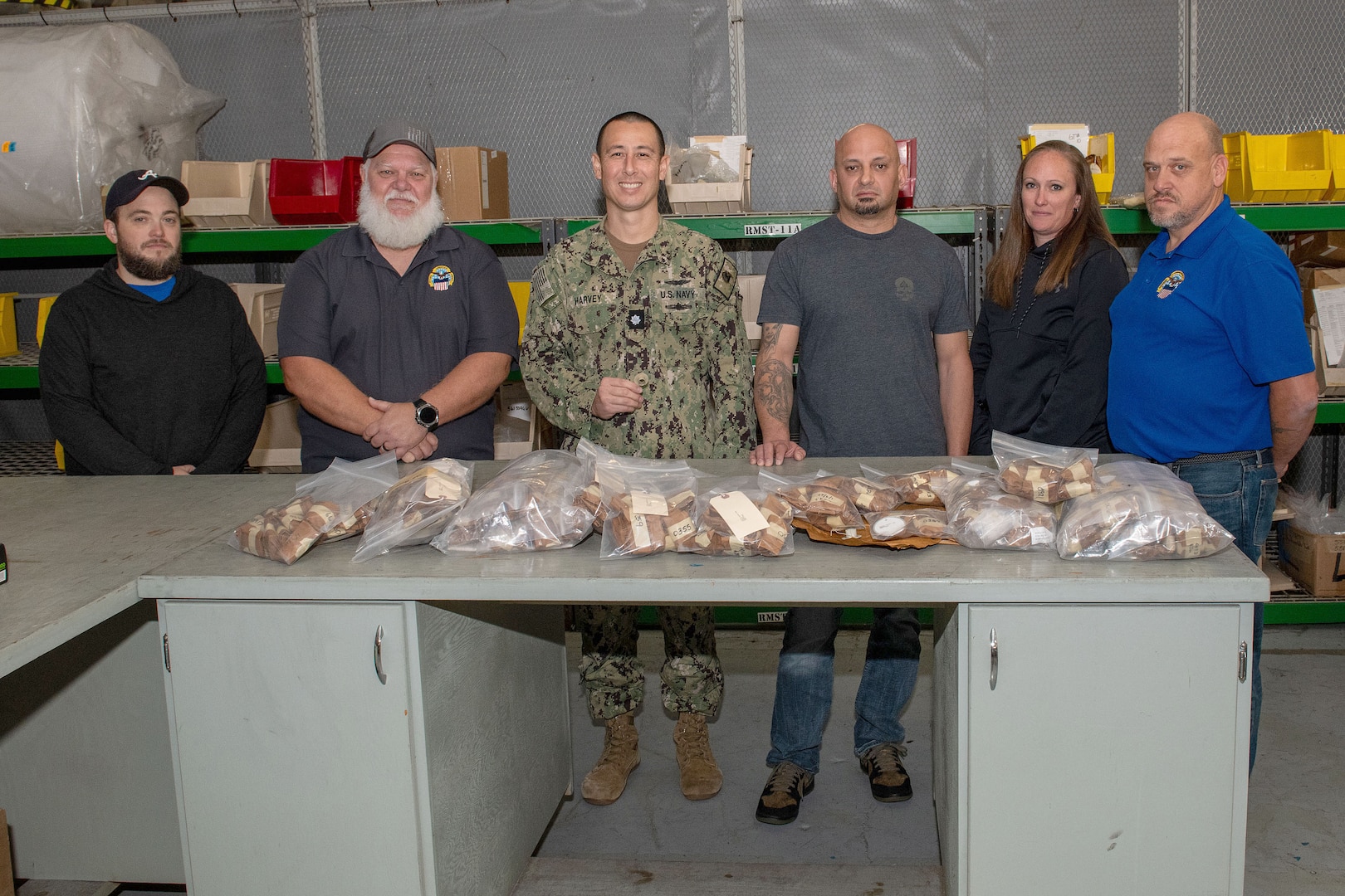 A group of people pose in front of helicopter parts in bags.