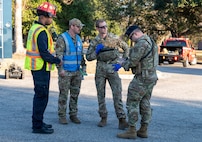 Four airmen stand, speaking to each other in the middle of the road.