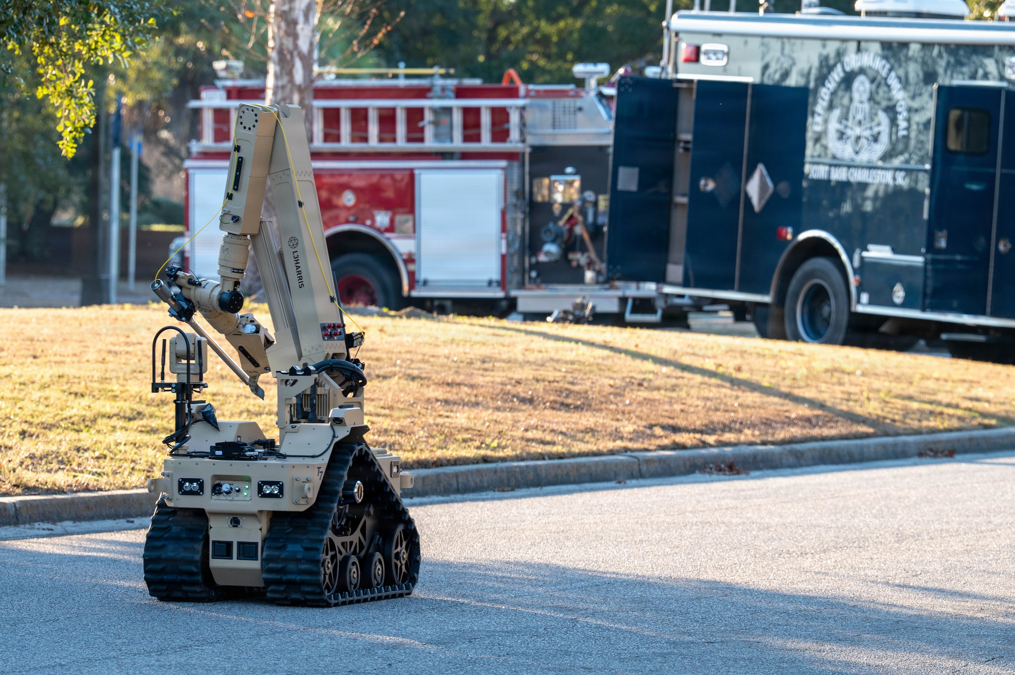 A robot drives in the road toward a firetruck and a large blue truck.