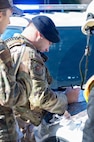 An Airman looks down at a map  while he writes on it on the hood of a car with police lights above him.