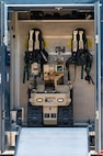 A compact tan robot sits behind an open doorway with equipment hanging behind it