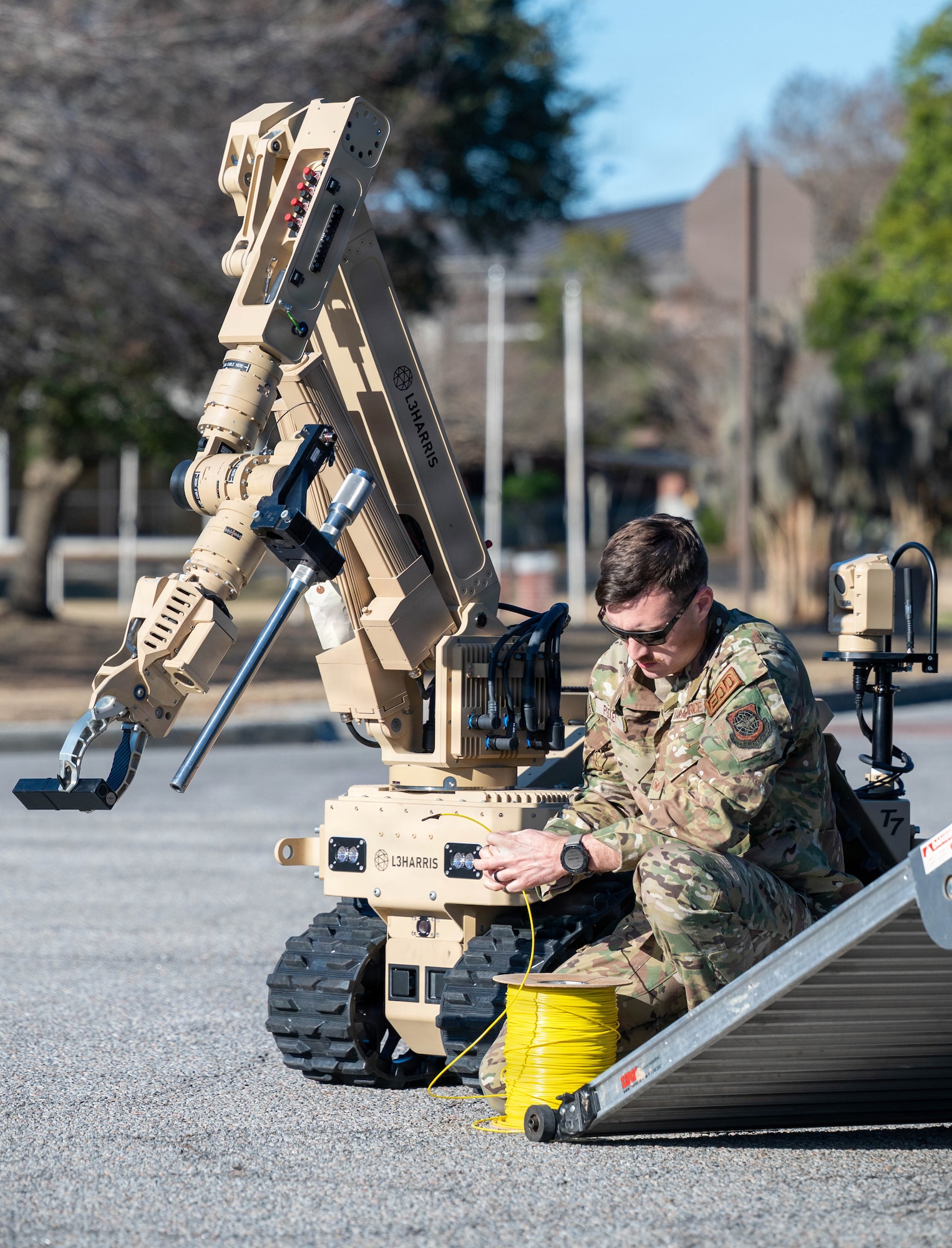 An Airman kneels beside a robot attaching a yellow wire to the base.