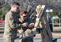 Two Airmen look at the arm of a robot, one reaches for it.