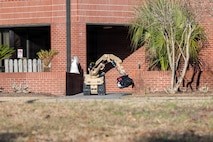A tan robot holds a backpack in the air perpendicular to the ground.