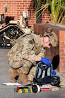 An Airman with a helmet and vest on examines the contents of a backpack with items all around him.