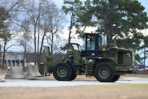 A forklift places a concrete barrier in the entryway of a parking lot.
