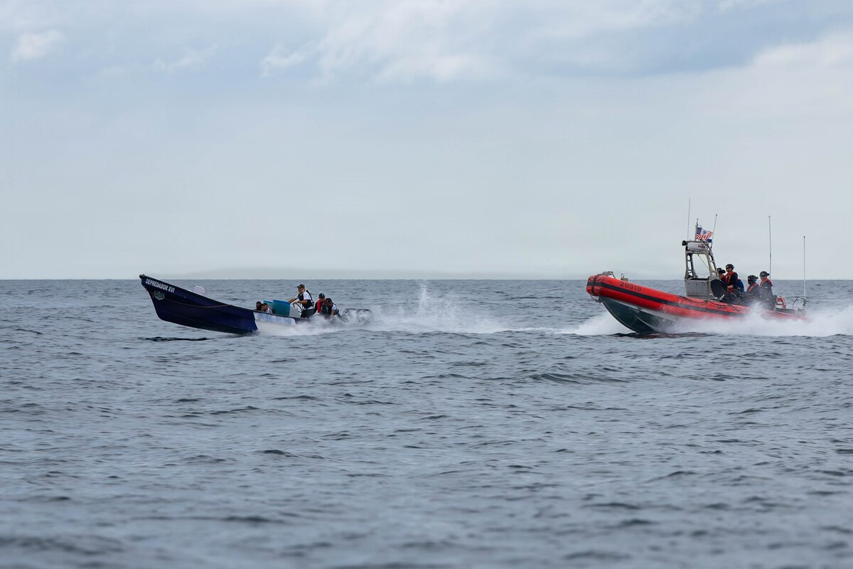 A small U.S. Coast Guard boat with people in camouflage military uniforms chases another small boat sailing in the water.
