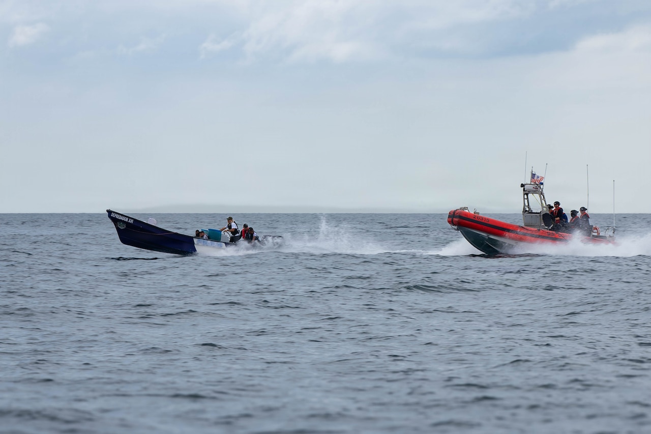 A small U.S. Coast Guard boat with people in camouflage military uniforms chases another small boat sailing in the water.