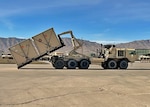 A container is loaded up onto an Army transport on a tarmac.