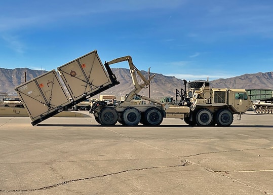 A container is loaded up onto an Army transport on a tarmac.